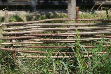 Kırsal bir çitin bir parçası. Kahverengi ahşap dallardan yapılmış. Yeşil otlarla kaplanmış.