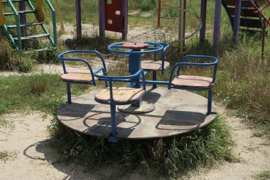 Yerde yuvarlak bir atlıkarınca ve sokakta yeşil çimenler olan çocuk parkı.