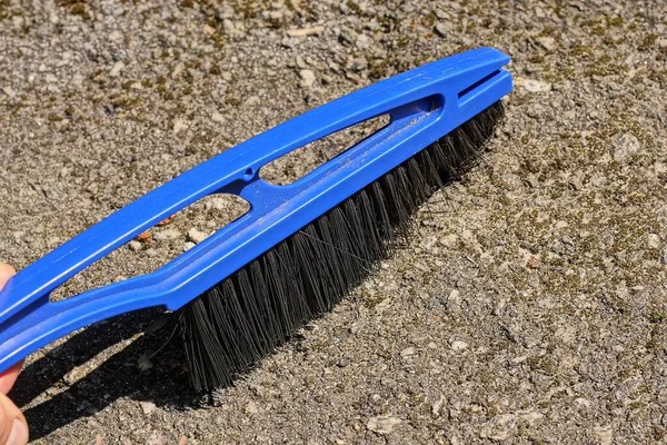 hand with a blue black plastic brush sweeps dust and debris from gray asphalt on the street