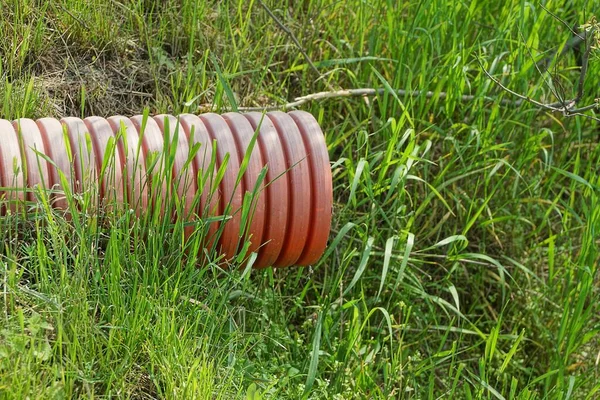Jedna Duża Czerwona Plastikowa Rura Kanalizacyjna Zielonej Trawie Ulicy — Zdjęcie stockowe