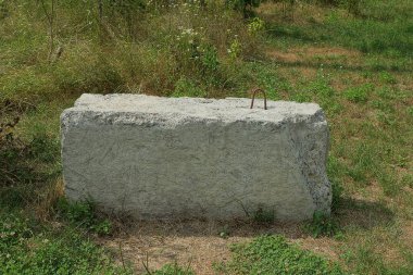 Büyük gri beton bir blok yerde ve yeşil çimenler dışarıda duruyor.