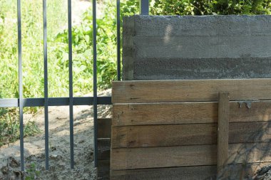 Gri beton bir temele dayanan tahtalardan yapılmış kahverengi ahşap bir yapının parçası. Sokakta bir çitin metal parmaklıklarının yanında.