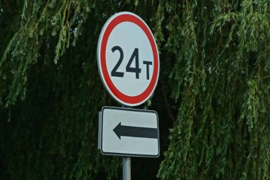 24 ton ağırlığı sınırlayan iki yol işareti ve yeşil bitki örtüsünün arka planına karşı sokakta bir ok.