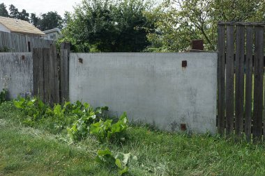 Gri tahta levhalardan yapılmış bir çitin kırsal duvarı ve yeşil çimenlerin içindeki ahşap tahtalar.