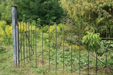 Dışarıda yeşil bitki örtüsü ve çimenlikte demir çubuklardan yapılmış siyah metal bir duvar.