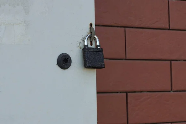 外の茶色のレンガの壁に向かって灰色の金属製のドアにかかっている黒い鉄の南京錠 — ストック写真