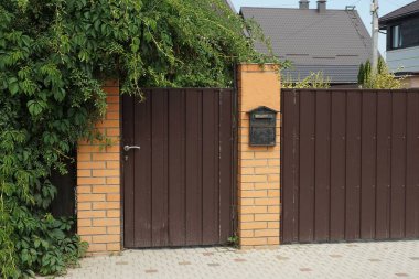 Kahverengi metal kapı ve duvarın bir kısmı demir ve tuğladan yapılmıştı.