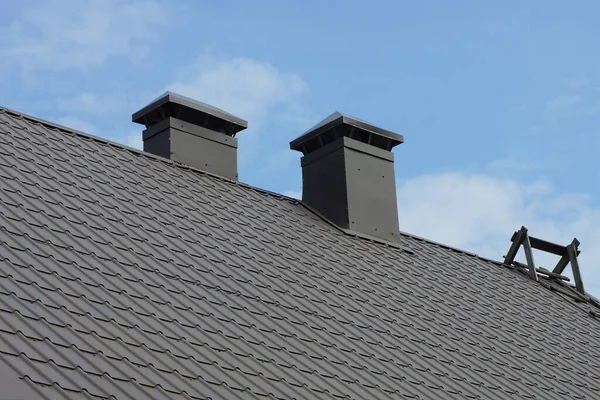 青い空に面した民家の灰色の瓦屋根の上に黒い金属製の煙突が2つ — ストック写真
