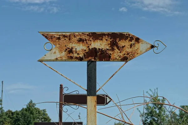 Eski bir gri metal ok levhası. Kahverengi pas içinde. Sokakta mavi gökyüzüne karşı.