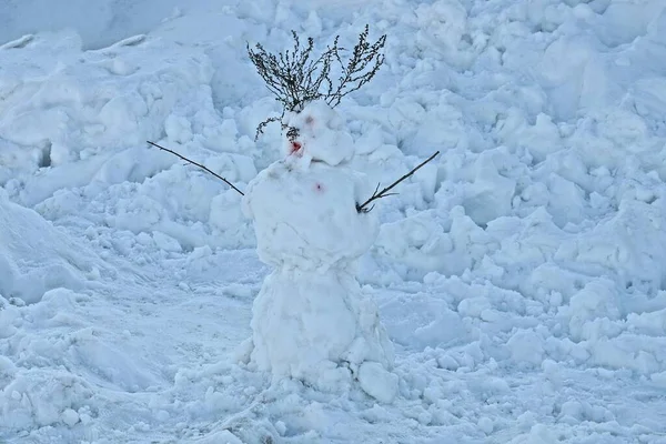 灰色の枝を持つ1人の雪だるまが夜の冬の通りに白い雪のドリフトの間に立っています — ストック写真