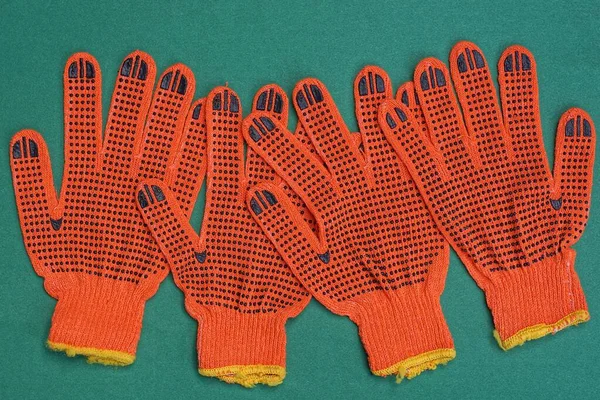 Kumaştan yapılmış dört kırmızı iş eldiveni yeşil bir masada yatıyor.