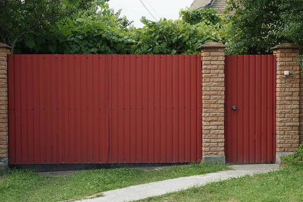 Büyük Kırmızı Metal Bir Kapı Yeşil Çimenlerdeki Kırsal Bir Sokakta — Stok fotoğraf