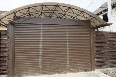 Kahverengi kapılı garaj cephesi ve sokaktaki ahşap çitin bir parçası.