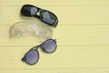 Üç beyaz siyah plastik güneş gözlüğü sarı ahşap bir masanın üzerinde duruyor.