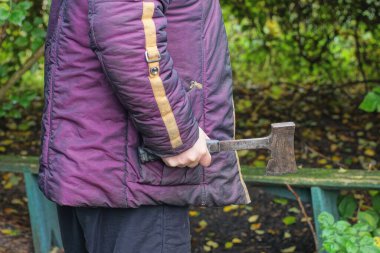 Mor elbiseli bir erkek işçi sokakta elinde gri bir balta tutuyor.