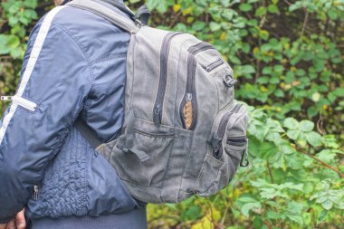 Bir tam gri sırt çantası, bahar caddesinde mavi ceketli bir adamın sırtında asılı.