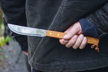 Siyah elbiseli bir erkek suçlunun eli ve sırtından bıçaklanmış gri kahverengi uzun bir caddenin ortasında.