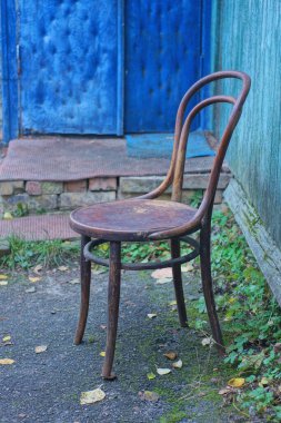 Eski kahverengi ahşap bir sandalye asfaltta duruyor Yazlık bir sokakta yeşil duvarın yanında