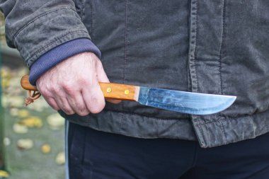 Sonbahar sokağında elinde eski bir bıçak tutan siyah ceketli bir adam var.