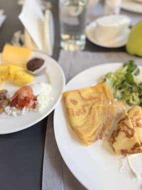 Lokantada kahvaltı taze meyve ve sebzelerle krep ve diyet yemekle masada iki beyaz tabakta.