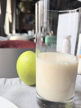Bir bardak beyaz sütün kahvaltısı ve masadaki yeşil elma.