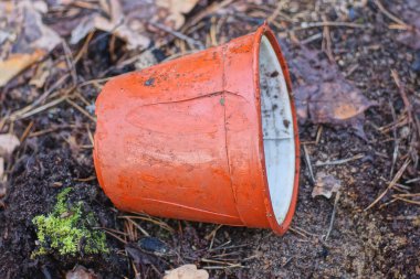 Kahverengi, kırık plastik bir saksıdan dökülen çöpler yerde yatar ve doğada dökülen yapraklar