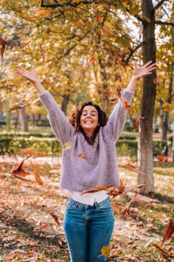 Güneşli bir sonbahar gününde güzel bir esmer kadın parkta yapraklarla eğleniyor. Sonbaharda açık havada yaşam tarzı