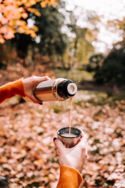 Güneşli bir sonbahar gününde mermer tırnaklı bir kadın fincana kahve döküyor. Yaşam tarzı ve dışarıda sonbahar pikniği. Kapat.