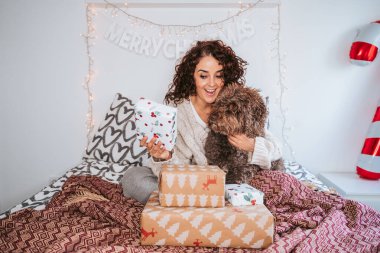 Güzel bir kadın İspanyol su köpeğiyle yatakta oturuyor ve Noel günü hediyeleri açmaya hazırlanıyor. O, evcil hayvanına bir hediye gösteriyor. Noel 'de köpeği olan aile kavramı