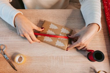 Kadın elleri Noel hediyesini kırmızı kurdeleyle süslüyor. Noel hediyeleri paketleme konsepti. Kapatın. Üst görünüm.