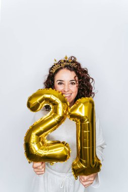 Güzel bir kadın büyük bir gülümsemeyle kameraya bakıyor ve elinde iki büyük altın balon tutuyor. Yeni yıl için 21 numara. Yeni yıl partisi ev kavramında