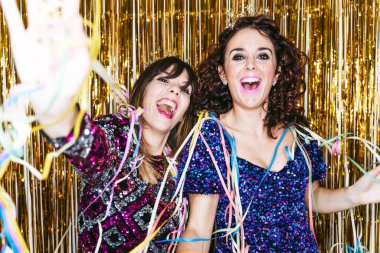 Arkalarında zarif kıyafetler ve dekorasyonlar giymiş iki güzel esmer kadın yıl sonunu birlikte kutlarken birkaç flamayla oynuyorlar. Yeni yıl partisi ev kavramında