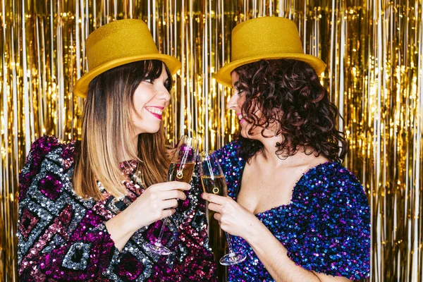 年底的时候 两个漂亮的女人穿着华丽的衣服 头戴金色的帽子 互相望着对方 用香槟酒敬酒 除夕夜家常便饭 — 图库照片