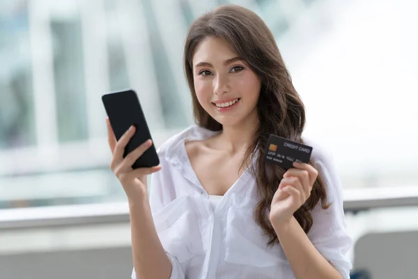 Black Friday concept, Woman holding phone with credit card and smiling near the store during shopping process