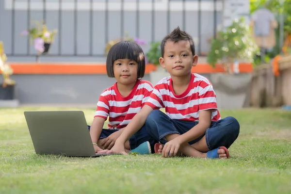 小可爱的亚洲男孩和女孩一起使用笔记本电脑 看相机 看卡通片或在网上玩耍 姐姐和哥哥坐在家里的操场上 — 图库照片