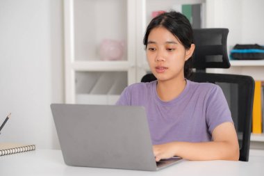 Genç bir kadın ev ofis ortamında bilgisayarında çalışırken görülüyor, dikkatlice ekrana bakıyor.