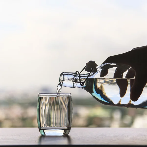 Un vaso de agua con una botella sobre la mesa —  Fotos de Stock