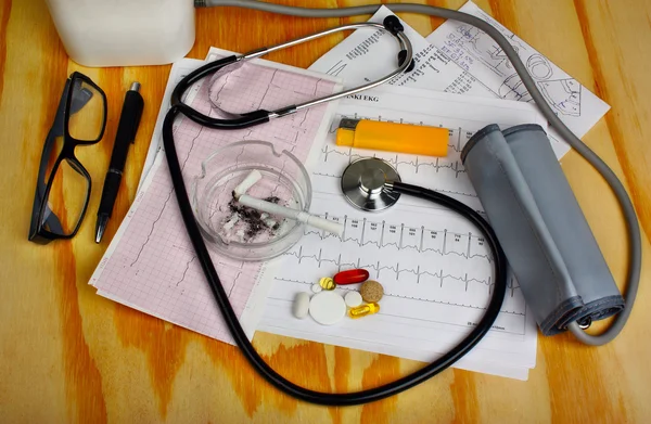 Cigarette in the ashtray and stethoscope, blood pressure monitor, pills — Stock Photo, Image