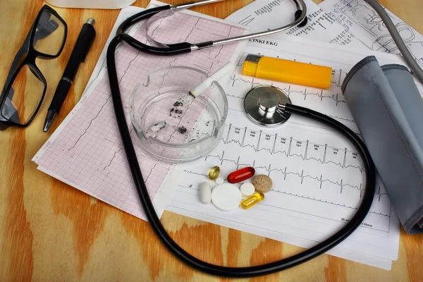 Cigarette in the ashtray and stethoscope, blood pressure monitor, pills — Stock Photo, Image