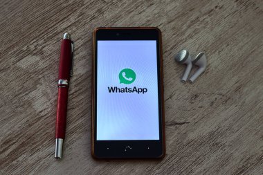 PRAT de LLOBREGAT, SPAIN - 25 Ekim 2020: Whatsapp logosu olan cep telefonu, ve bir kalem ve kulaklıkla birlikte ahşap bir masa üzerinde açık uygulama