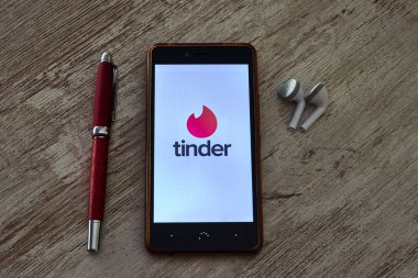 PRAT DE LLOBREGAT, SPAIN - 25 EKİM 2020 Tinder logosu olan cep telefonu ve bir kalem ve kulaklıkla birlikte ahşap bir masa üzerinde açık uygulama