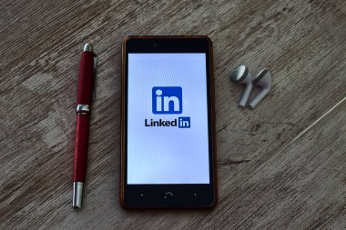PRAT DE LLOBREGAT, SPAIN - 25 EKİM 2020: LinkedIn logosu olan cep telefonu, ve bir kalem ve kulaklıkla birlikte ahşap bir masa üzerinde açık uygulama