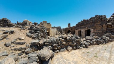 Antik taş kalıntıları berrak mavi bir gökyüzü altında, tarihi mimari sergileniyor. Bosra antik, Suriye