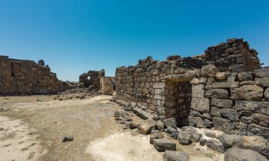 Eski taş kalıntıları berrak mavi bir gökyüzünün altında dağınık kayalar ve kirli bir patika var. Bosra antik, Suriye
