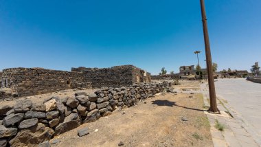 Kadim taş kalıntıları berrak mavi bir gökyüzünün altında asfalt bir geçitle birlikte. Bosra antik, Suriye