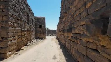 Açık mavi gökyüzünün altında kaldırım taşı yolu olan antik taş kalıntıları. Bosra antik, Suriye