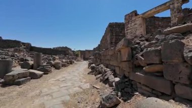 Açık mavi gökyüzünün altında harabeleri ve sütunları olan antik Roma yolu. Bosra antik, Suriye