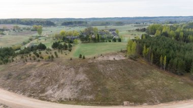 Aerial view of a rural landscape featuring a mix of fields, forests, and a few houses in the distance