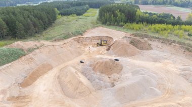 Ağır makineler ve kum yığınlarıyla dolu bir kum ocağının havadan görünüşü.