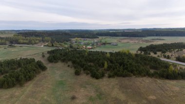 Aerial view of a rural landscape featuring fields, scattered trees, and small farmhouses in the distance under a cloudy sky